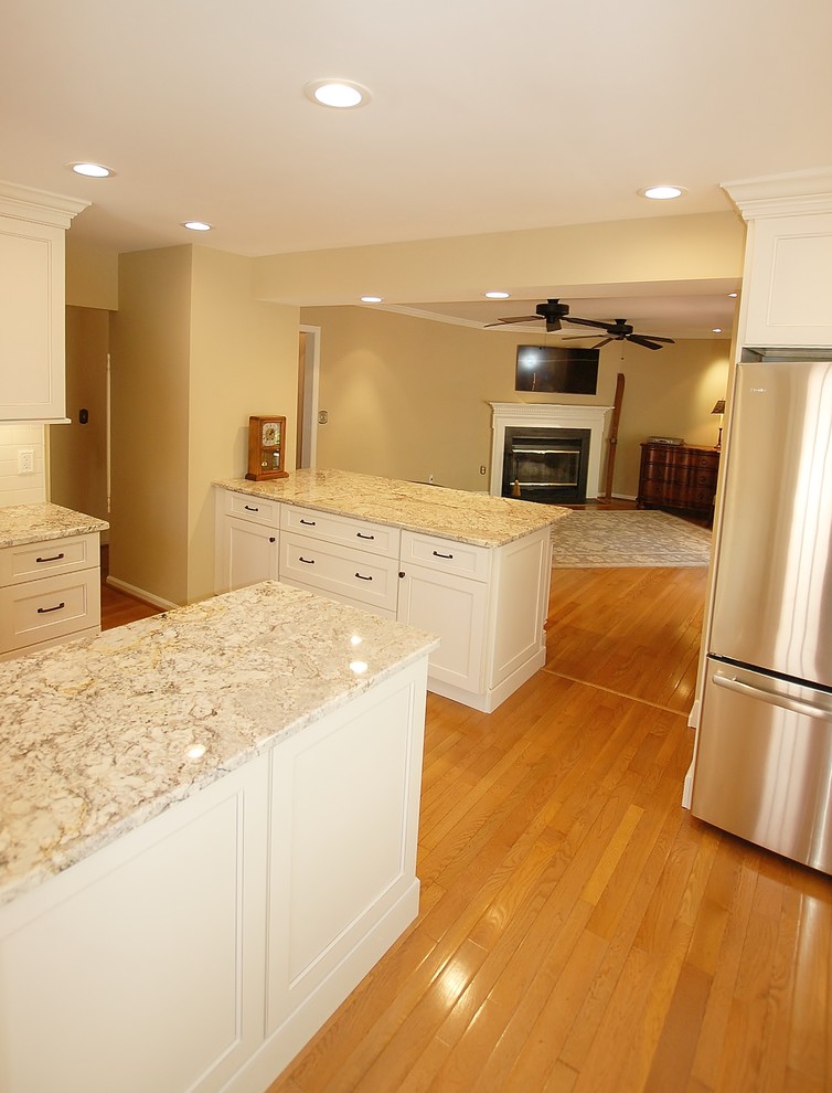 Mid-sized transitional l-shaped light wood floor eat-in kitchen photo in Philadelphia with an undermount sink, raised-panel cabinets, white cabinets, granite countertops, white backsplash, subway tile backsplash, stainless steel appliances and an island