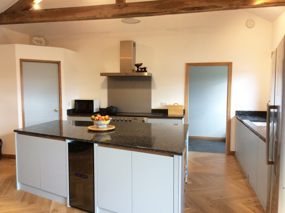 Photo of a medium sized contemporary l-shaped kitchen/diner in London with flat-panel cabinets, grey cabinets, quartz worktops, grey splashback, light hardwood flooring, an island, brown floors and black worktops.