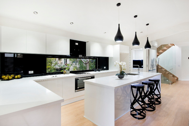 Offene Moderne Küche in L-Form mit Unterbauwaschbecken, flächenbündigen Schrankfronten, weißen Schränken, Rückwand-Fenster, Küchengeräten aus Edelstahl, Sperrholzboden und Kücheninsel in Brisbane