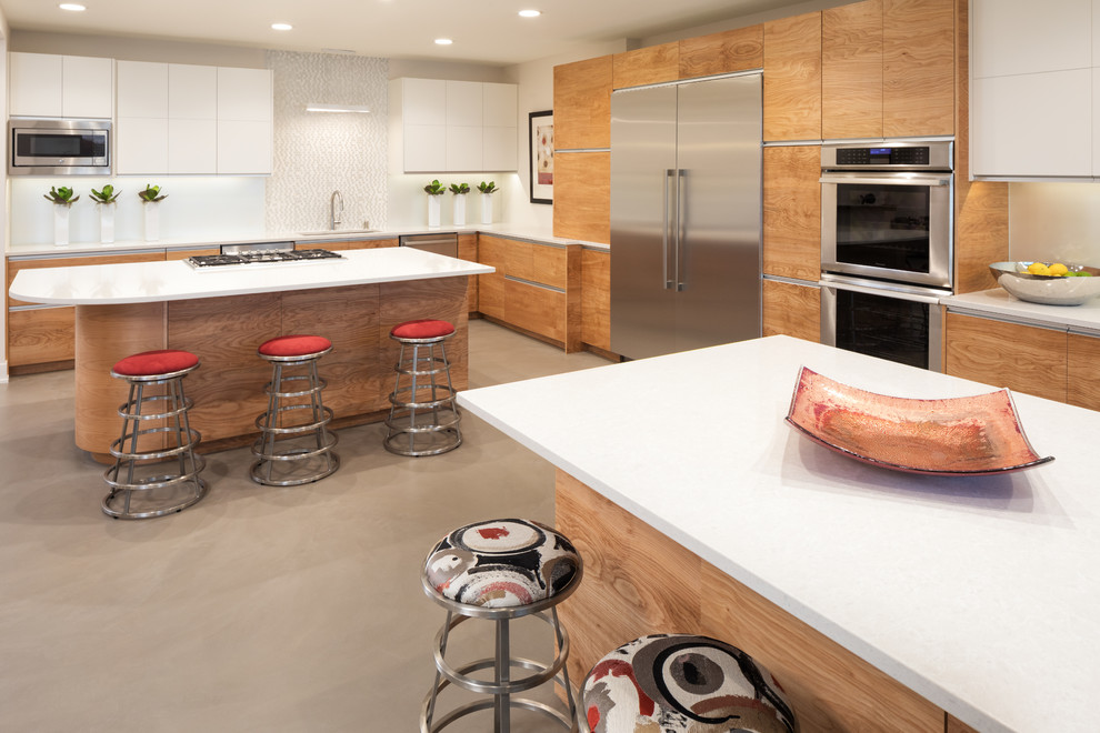 Kitchen - large contemporary l-shaped concrete floor and gray floor kitchen idea in Minneapolis with an undermount sink, flat-panel cabinets, quartz countertops, white backsplash, glass sheet backsplash, stainless steel appliances, two islands and medium tone wood cabinets