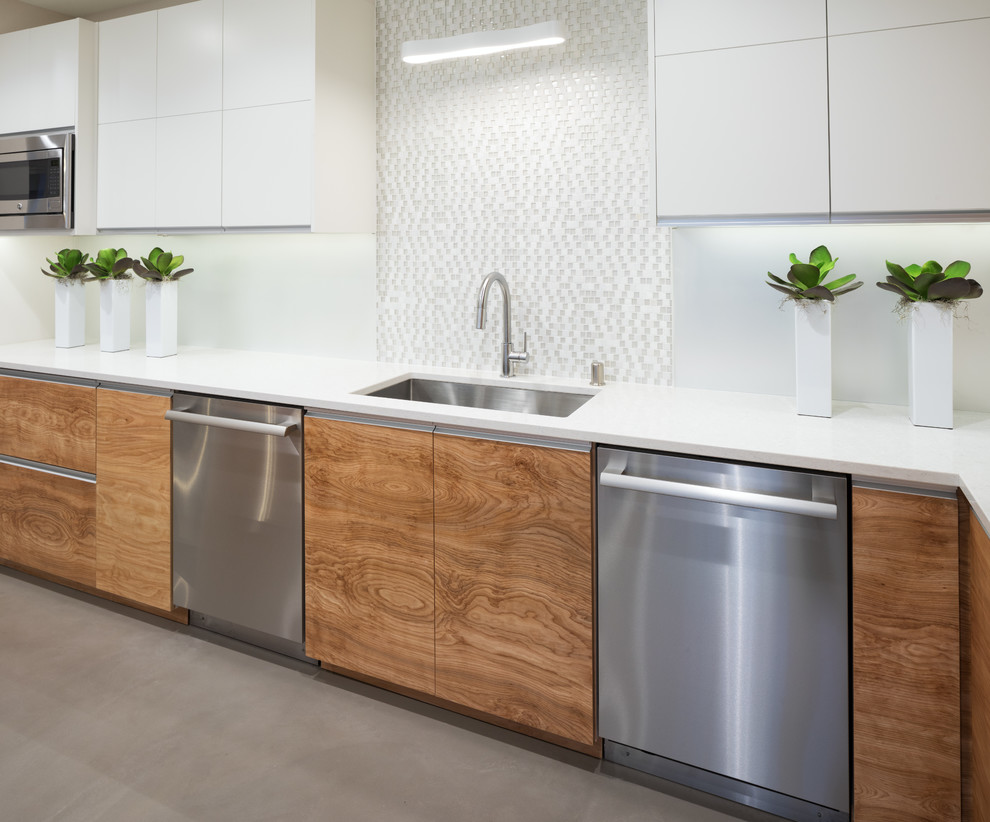 Photo of a large contemporary l-shaped kitchen in Minneapolis with a submerged sink, flat-panel cabinets, white cabinets, engineered stone countertops, white splashback, glass sheet splashback, stainless steel appliances, concrete flooring, multiple islands and grey floors.
