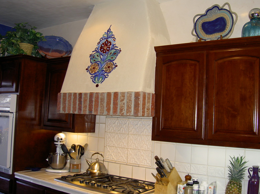 Design ideas for a kitchen in Albuquerque with raised-panel cabinets, dark wood cabinets, tile countertops, white splashback, ceramic splashback and white appliances.