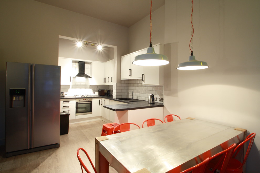 This is an example of a medium sized industrial u-shaped kitchen/diner in London with a single-bowl sink, white cabinets, white splashback, metro tiled splashback, stainless steel appliances and lino flooring.