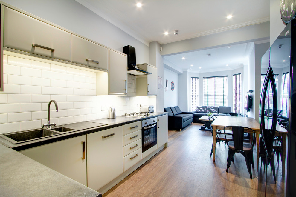 Medium sized urban l-shaped kitchen/diner in London with a double-bowl sink, white splashback, metro tiled splashback, stainless steel appliances and lino flooring.