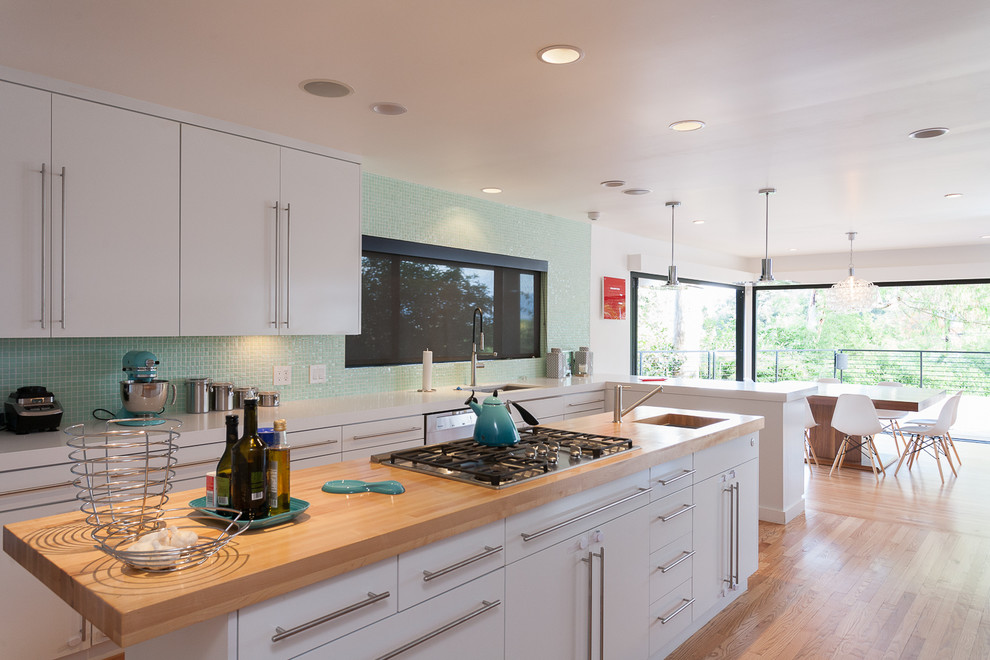 Modern inredning av ett kök, med en undermonterad diskho, släta luckor, vita skåp, blått stänkskydd, stänkskydd i mosaik, ljust trägolv och en köksö