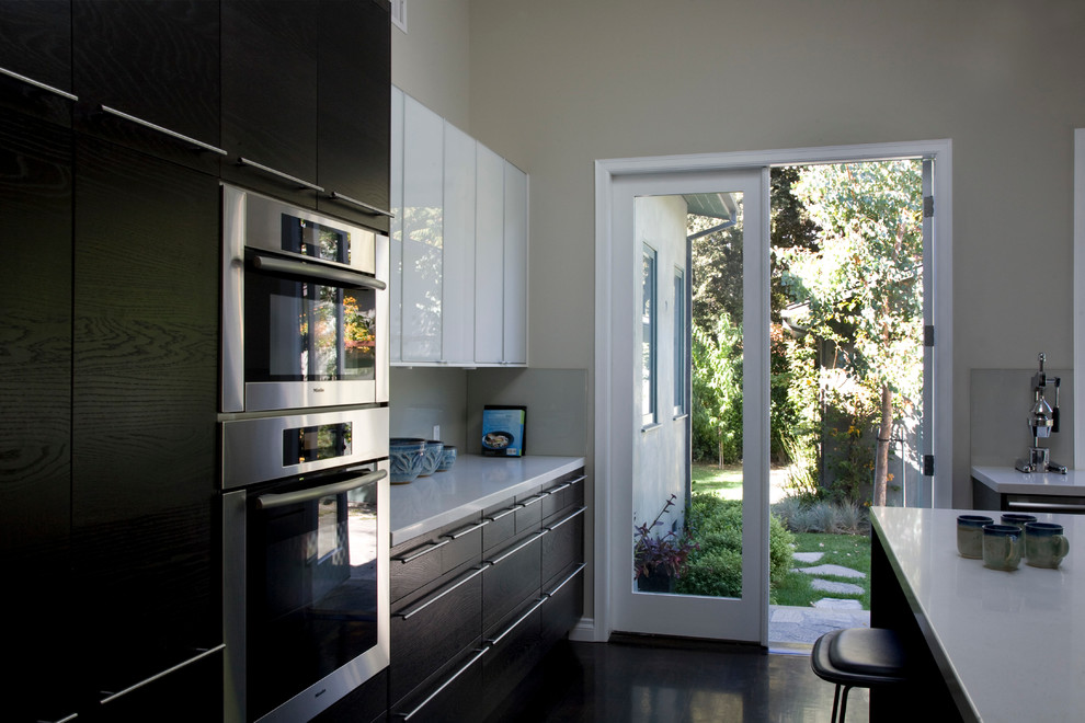Inspiration for a medium sized contemporary l-shaped enclosed kitchen in Los Angeles with a submerged sink, flat-panel cabinets, white cabinets, stainless steel worktops, beige splashback, glass sheet splashback, stainless steel appliances, dark hardwood flooring and an island.