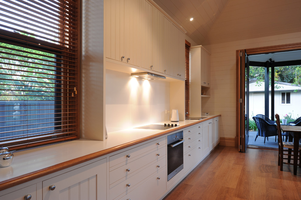 Bild på ett mellanstort funkis linjärt kök med öppen planlösning, med en enkel diskho, luckor med infälld panel, vita skåp, träbänkskiva, vitt stänkskydd, rostfria vitvaror och mellanmörkt trägolv