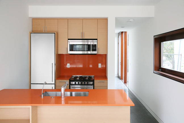 Idee per una piccola cucina design con lavello sottopiano, ante lisce, ante beige, top in superficie solida, paraspruzzi arancione, elettrodomestici in acciaio inossidabile, pavimento in cemento, penisola e pavimento grigio