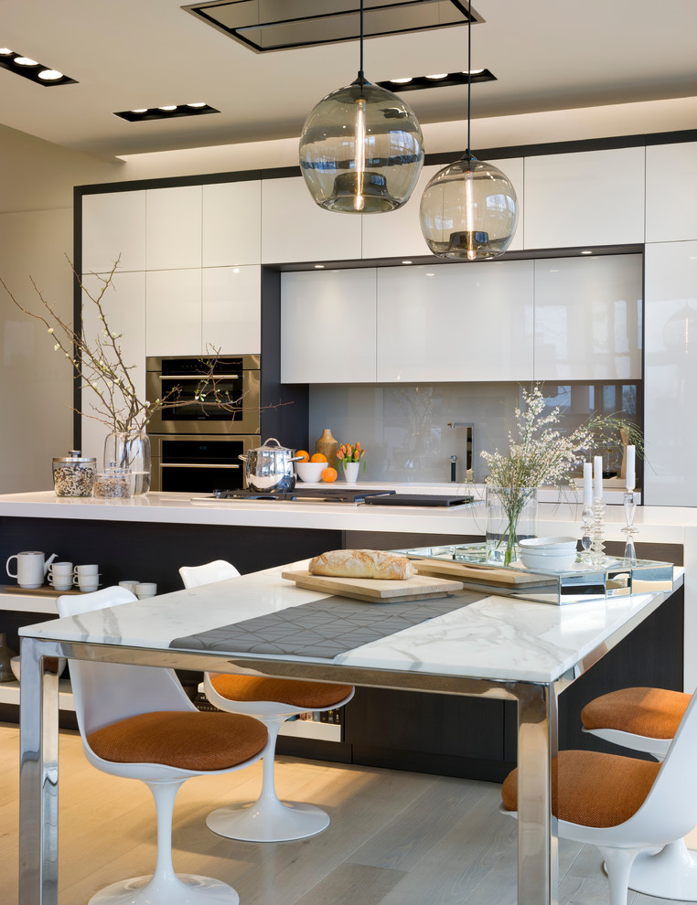 Immagine di una cucina minimalista con ante lisce, ante bianche, parquet chiaro, lavello sottopiano, paraspruzzi grigio, paraspruzzi con lastra di vetro e elettrodomestici da incasso