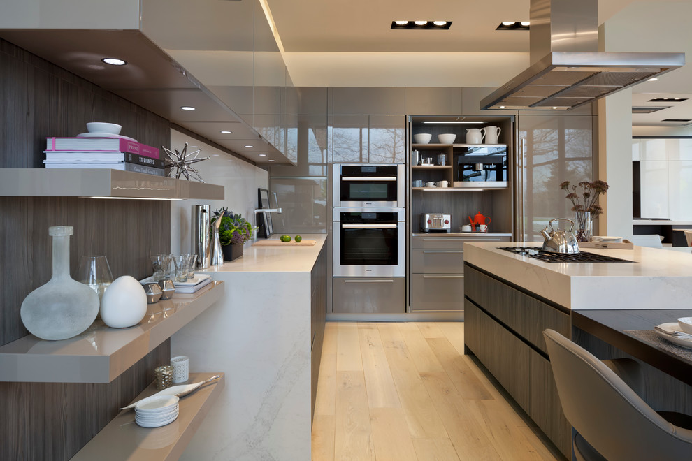 Contemporary kitchen/diner in DC Metro with flat-panel cabinets, white splashback, light hardwood flooring, an island, a submerged sink, beige cabinets, stone slab splashback and integrated appliances.
