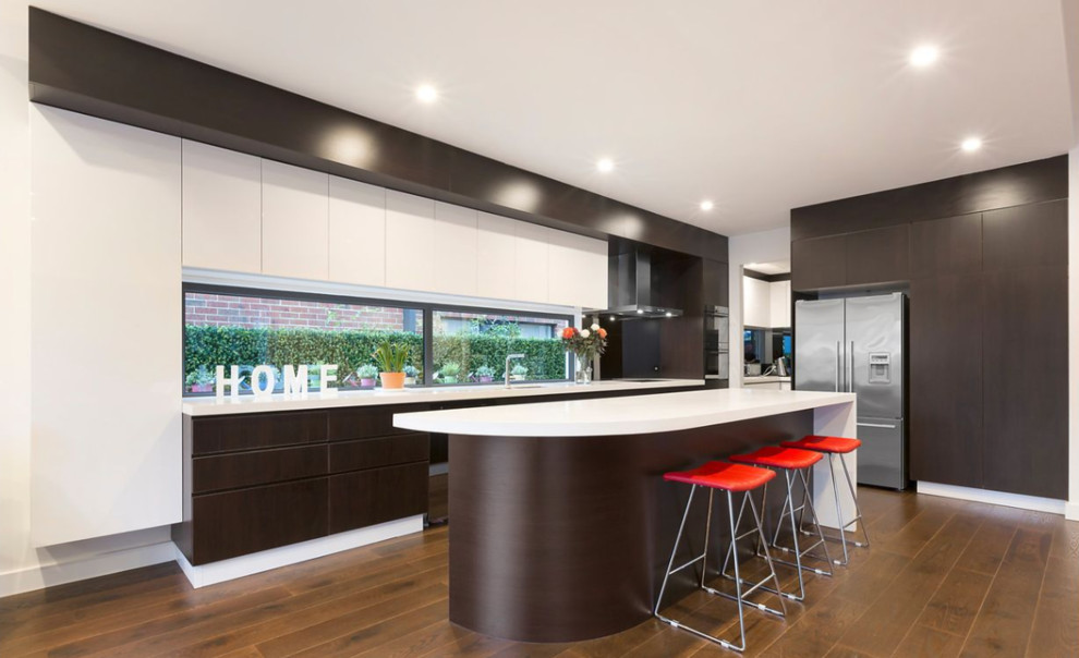 Moderne Küche mit Unterbauwaschbecken, flächenbündigen Schrankfronten, braunen Schränken, Rückwand-Fenster, Küchengeräten aus Edelstahl, braunem Holzboden, Kücheninsel, braunem Boden und weißer Arbeitsplatte in Melbourne