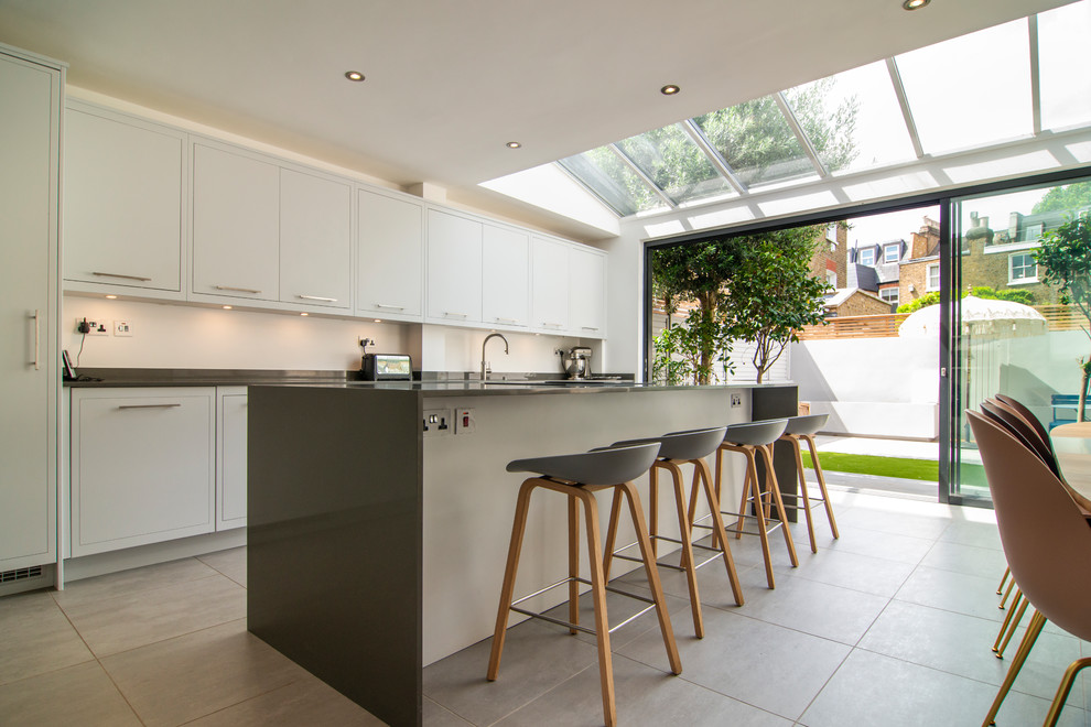 Bild på ett mellanstort funkis grå linjärt grått kök och matrum, med släta luckor, vita skåp, en köksö och grått golv