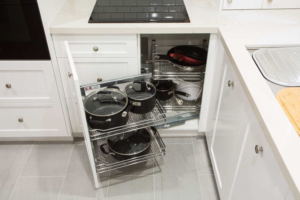 This is an example of a small traditional u-shaped kitchen pantry in Brisbane with a double-bowl sink, shaker cabinets, white cabinets, engineered stone countertops, grey splashback, ceramic splashback, black appliances, porcelain flooring, an island, grey floors and white worktops.