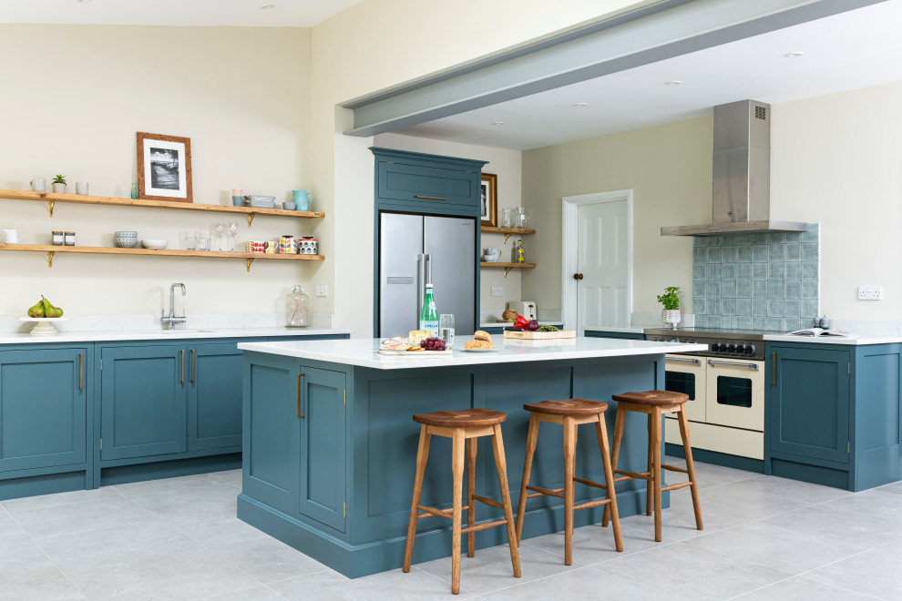 Photo of a medium sized traditional grey and teal l-shaped kitchen/diner in London with shaker cabinets, blue cabinets, quartz worktops, an island, white worktops, blue splashback, stainless steel appliances, grey floors and exposed beams.
