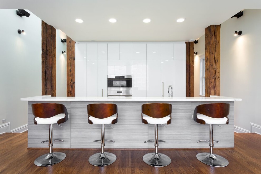 Idéer för stora funkis linjära kök och matrum, med en undermonterad diskho, släta luckor, vita skåp, marmorbänkskiva, integrerade vitvaror, mellanmörkt trägolv och en köksö