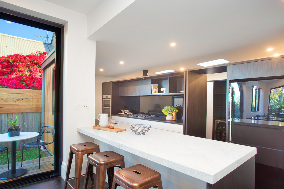 Inspiration for a contemporary single-wall enclosed kitchen in Sydney with flat-panel cabinets, brown cabinets, composite countertops, mirror splashback, stainless steel appliances, an island, white worktops, metallic splashback and brown floors.