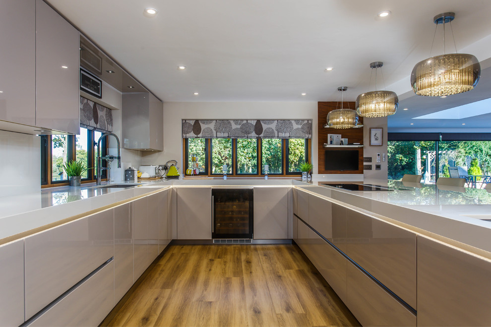 Design ideas for a contemporary u-shaped open plan kitchen in Sussex with a submerged sink, flat-panel cabinets, grey cabinets, white splashback, black appliances, medium hardwood flooring, brown floors and grey worktops.