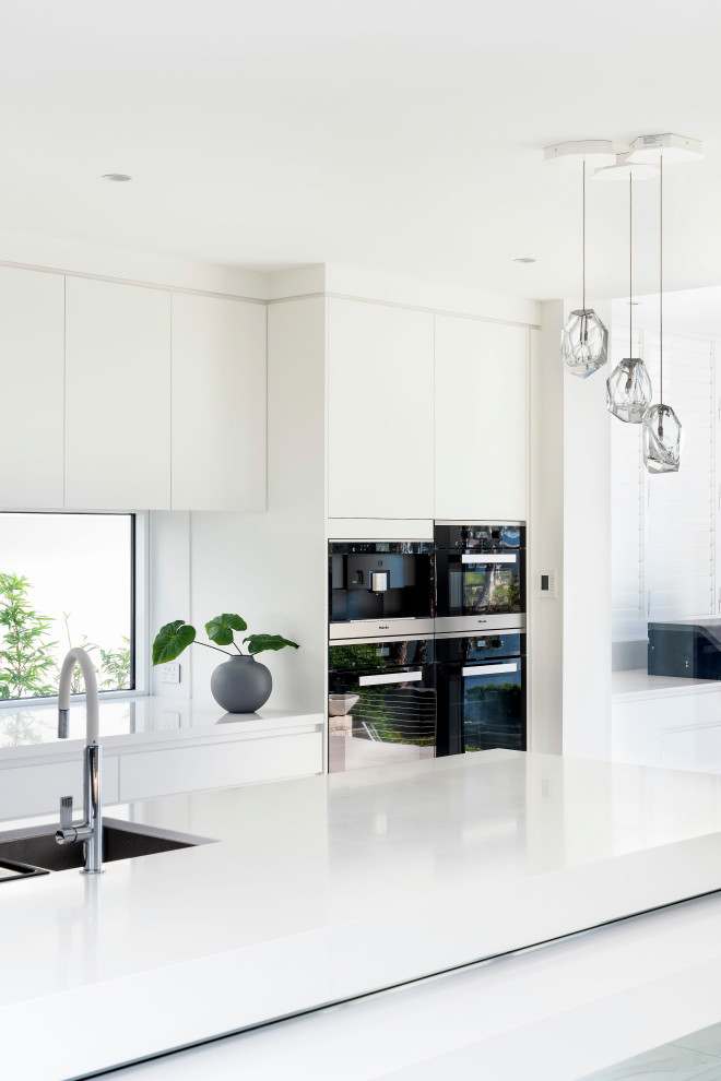 Zweizeilige, Geräumige Moderne Küche mit weißen Schränken, Quarzwerkstein-Arbeitsplatte, schwarzen Elektrogeräten, Kücheninsel und weißer Arbeitsplatte in Sonstige