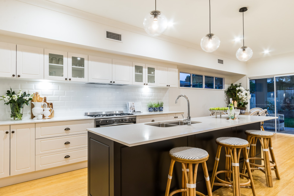 Large beach style galley light wood floor and yellow floor open concept kitchen photo in Brisbane with a double-bowl sink, shaker cabinets, black cabinets, quartz countertops, white backsplash, ceramic backsplash, stainless steel appliances, an island and white countertops