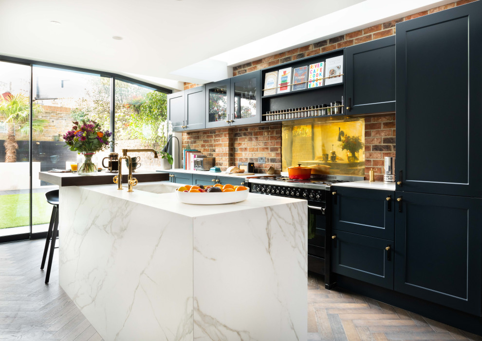 Inspiration for a traditional galley kitchen in London with a submerged sink, recessed-panel cabinets, red splashback, brick splashback, black appliances, dark hardwood flooring, an island, brown floors and white worktops.