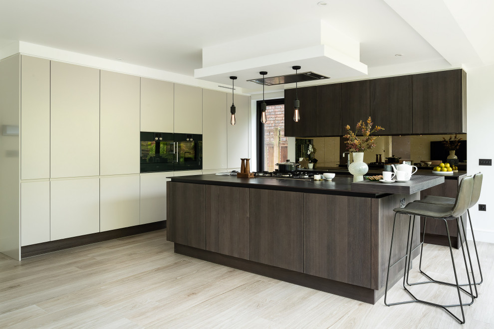 Trendy l-shaped light wood floor and beige floor kitchen photo in London with flat-panel cabinets, dark wood cabinets, black appliances, an island and black countertops