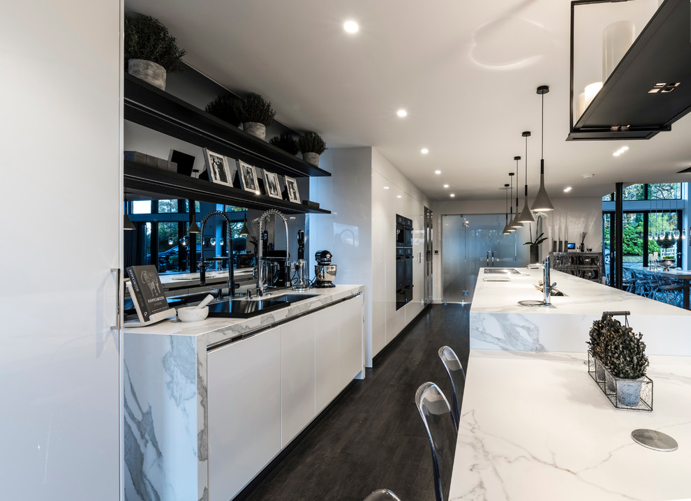 Große Moderne Küche mit flächenbündigen Schrankfronten, weißen Schränken, schwarzen Elektrogeräten, dunklem Holzboden und Kücheninsel in Cheshire