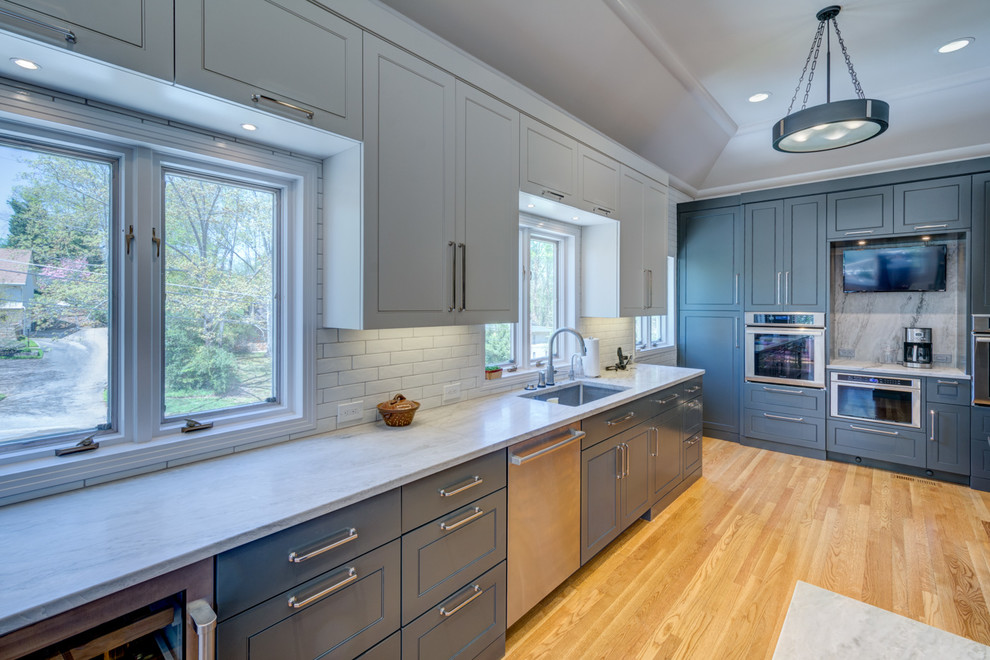 Large trendy u-shaped light wood floor and brown floor enclosed kitchen photo in Atlanta with an undermount sink, raised-panel cabinets, gray cabinets, quartzite countertops, white backsplash, subway tile backsplash, stainless steel appliances, a peninsula and white countertops