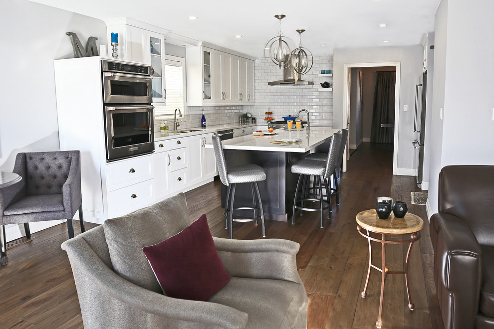 Bild på ett stort funkis kök, med en undermonterad diskho, skåp i shakerstil, vita skåp, bänkskiva i kvarts, vitt stänkskydd, stänkskydd i keramik, rostfria vitvaror, mellanmörkt trägolv, en köksö och brunt golv