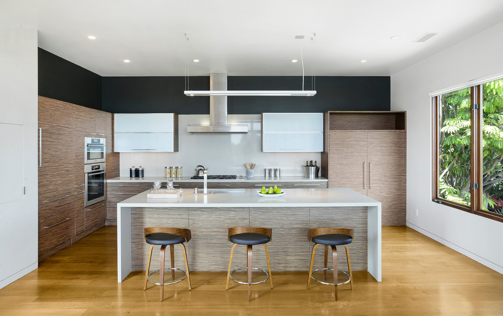 Foto di una cucina design con lavello sottopiano, ante lisce, paraspruzzi bianco, elettrodomestici in acciaio inossidabile, pavimento in legno massello medio e top bianco