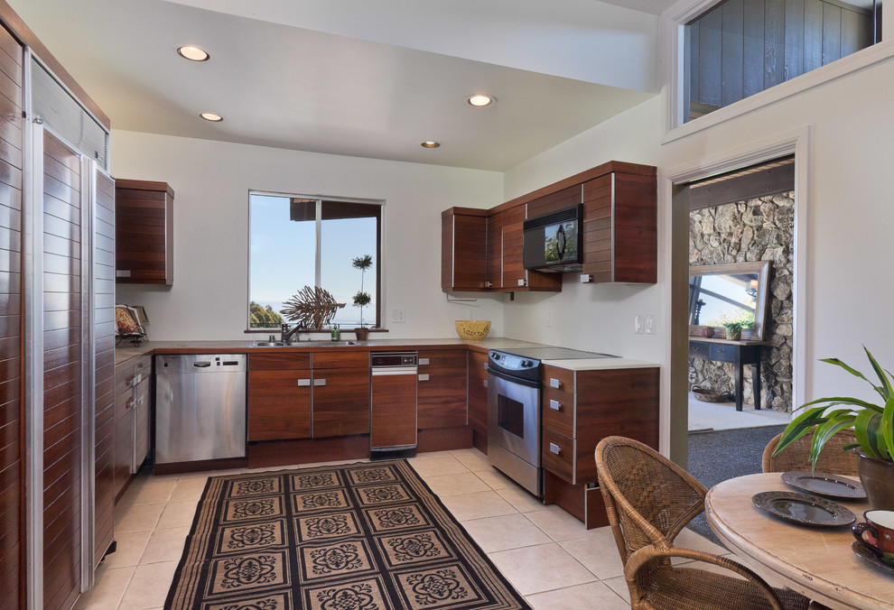 Photo of a beach style u-shaped kitchen/diner in Santa Barbara with a built-in sink, flat-panel cabinets, dark wood cabinets and stainless steel appliances.