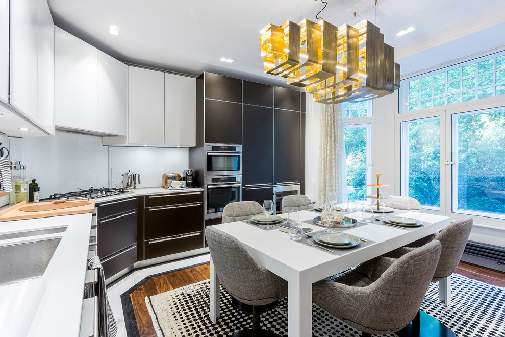 Eat-in kitchen - contemporary l-shaped medium tone wood floor eat-in kitchen idea in London with a double-bowl sink, flat-panel cabinets, white backsplash, stainless steel appliances and white countertops