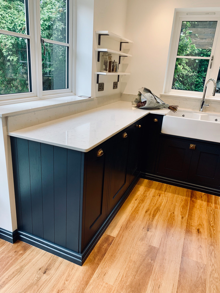 Design ideas for a large contemporary l-shaped kitchen/diner in Other with a belfast sink, shaker cabinets, blue cabinets, quartz worktops, black appliances, medium hardwood flooring, an island, blue floors and white worktops.
