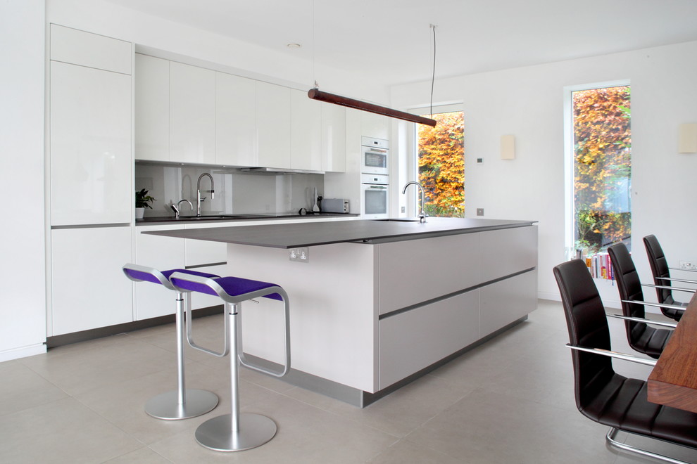 Exemple d'une cuisine parallèle moderne avec un placard à porte plane, des portes de placard blanches, une crédence grise, îlot, un sol gris et plan de travail noir.