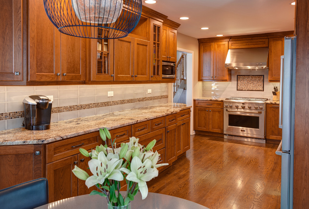 Mid-sized transitional l-shaped medium tone wood floor kitchen photo in Chicago with an undermount sink, flat-panel cabinets, medium tone wood cabinets, granite countertops, beige backsplash, ceramic backsplash and stainless steel appliances