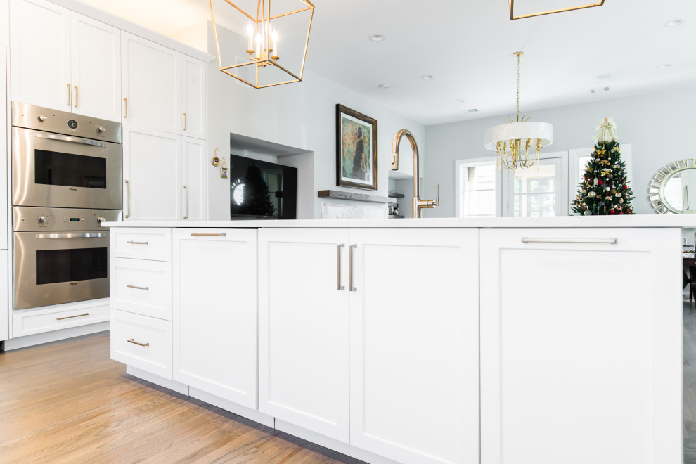Example of a large transitional l-shaped medium tone wood floor and brown floor open concept kitchen design in Dallas with an undermount sink, shaker cabinets, white cabinets, quartz countertops, beige backsplash, porcelain backsplash, stainless steel appliances, an island and white countertops
