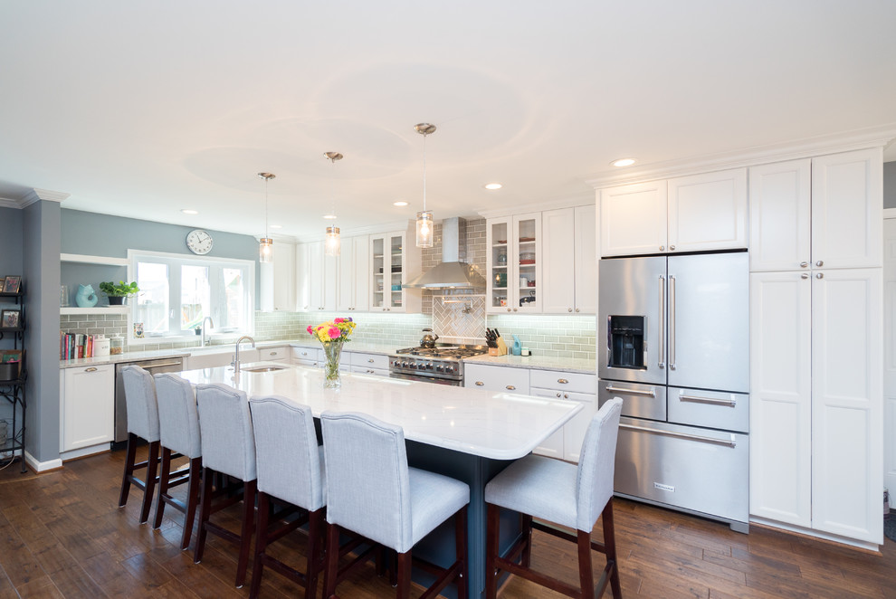 Inspiration for a large traditional l-shaped kitchen/diner in DC Metro with a belfast sink, shaker cabinets, white cabinets, engineered stone countertops, grey splashback, porcelain splashback, stainless steel appliances, dark hardwood flooring, an island and brown floors.