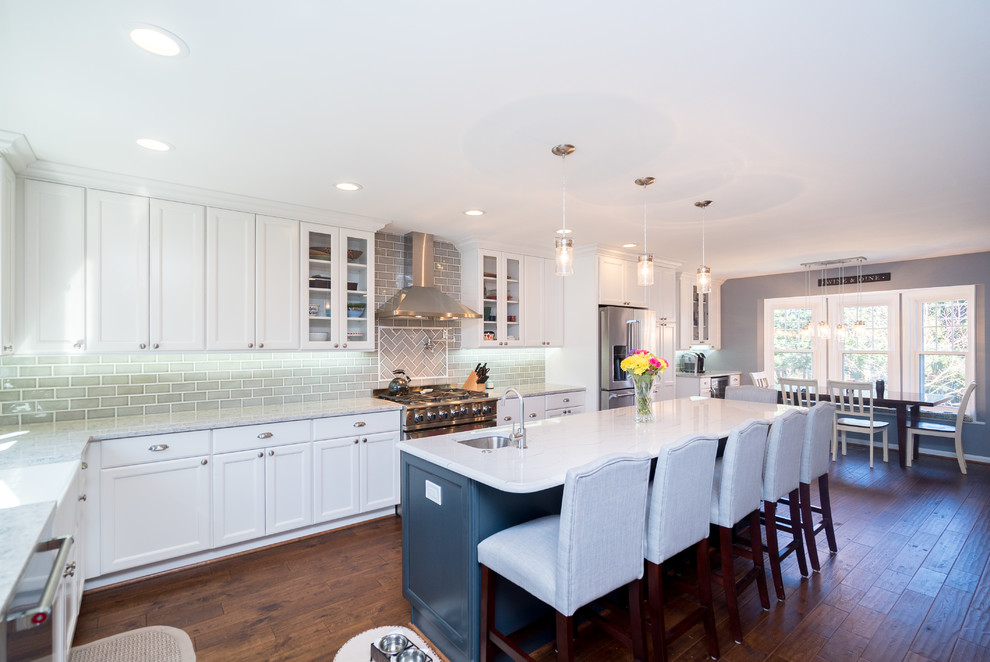 Inspiration for a large classic l-shaped kitchen/diner in DC Metro with a belfast sink, shaker cabinets, white cabinets, engineered stone countertops, grey splashback, porcelain splashback, stainless steel appliances, dark hardwood flooring, an island and brown floors.