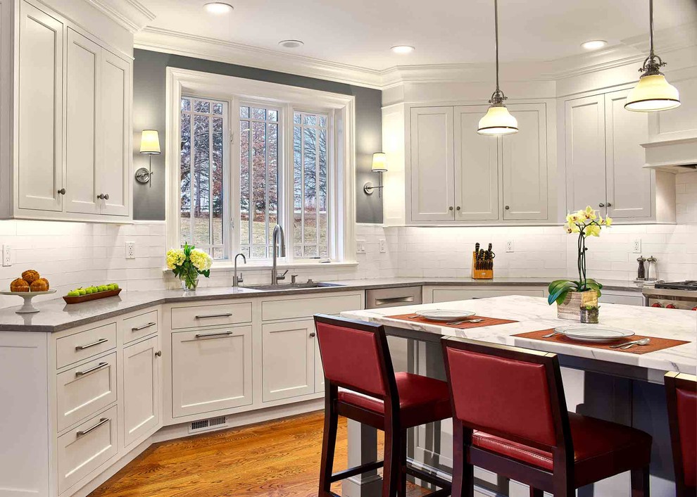 Inredning av ett klassiskt stort grå grått kök, med en nedsänkt diskho, luckor med profilerade fronter, vita skåp, bänkskiva i kalksten, vitt stänkskydd, stänkskydd i keramik, rostfria vitvaror, mellanmörkt trägolv, en köksö och brunt golv