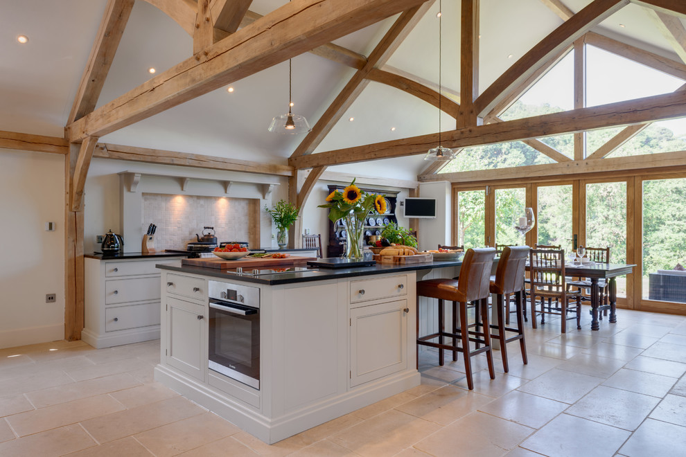 This is an example of a large rural single-wall kitchen in Other with recessed-panel cabinets, grey cabinets, beige splashback, stainless steel appliances, an island, beige floors and black worktops.