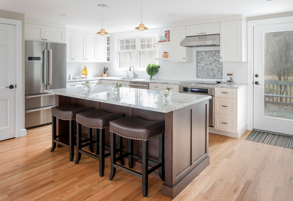 Inspiration for a large transitional l-shaped medium tone wood floor and brown floor enclosed kitchen remodel in Boston with an undermount sink, shaker cabinets, white cabinets, marble countertops, white backsplash, subway tile backsplash, stainless steel appliances and an island