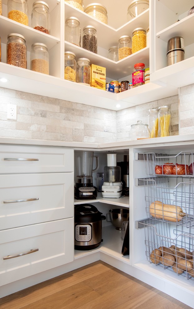 Large contemporary u-shaped kitchen pantry in Vancouver with a belfast sink, shaker cabinets, white cabinets, engineered stone countertops, grey splashback, marble splashback, stainless steel appliances, light hardwood flooring, an island, beige floors and white worktops.