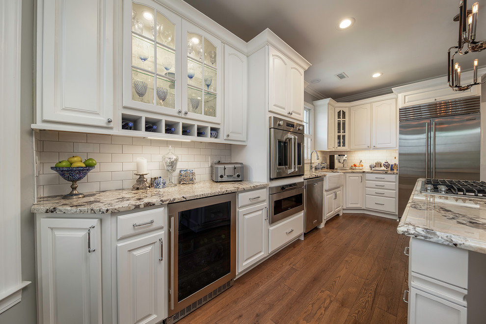 Eat-in kitchen - traditional eat-in kitchen idea in Other with a farmhouse sink, raised-panel cabinets, white cabinets, granite countertops, subway tile backsplash, stainless steel appliances and an island