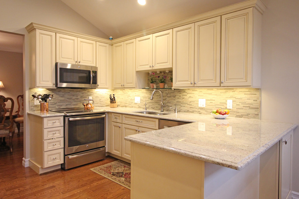 Klassisk inredning av ett mellanstort kök, med en undermonterad diskho, luckor med upphöjd panel, vita skåp, grått stänkskydd, stänkskydd i mosaik, rostfria vitvaror, mellanmörkt trägolv och en halv köksö