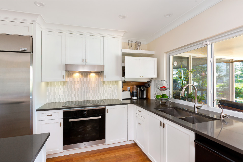 Photo of a contemporary l-shaped kitchen in Miami with shaker cabinets, white cabinets, engineered stone countertops, glass tiled splashback, medium hardwood flooring and an island.