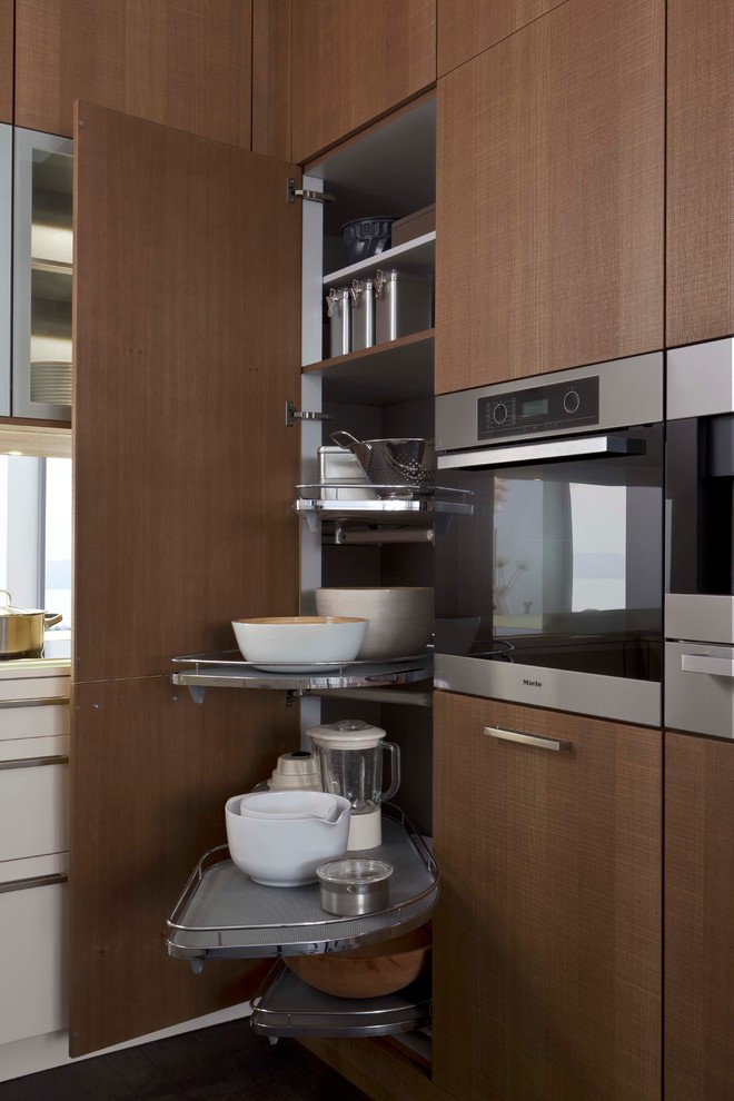 This is an example of a medium sized contemporary l-shaped kitchen/diner in New York with flat-panel cabinets, white cabinets, composite countertops, stainless steel appliances, light hardwood flooring and a breakfast bar.
