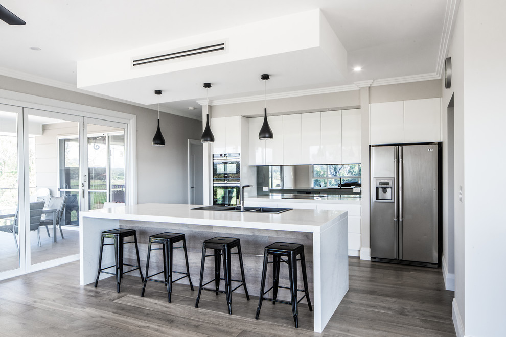 Large modern galley kitchen pantry in Sydney with a built-in sink, flat-panel cabinets, white cabinets, engineered stone countertops, black splashback, glass sheet splashback, stainless steel appliances, plywood flooring, an island and grey floors.