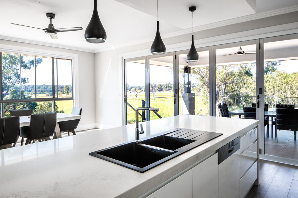 Inspiration for a large modern galley kitchen pantry in Sydney with a built-in sink, flat-panel cabinets, white cabinets, engineered stone countertops, black splashback, glass sheet splashback, stainless steel appliances, plywood flooring, an island and grey floors.
