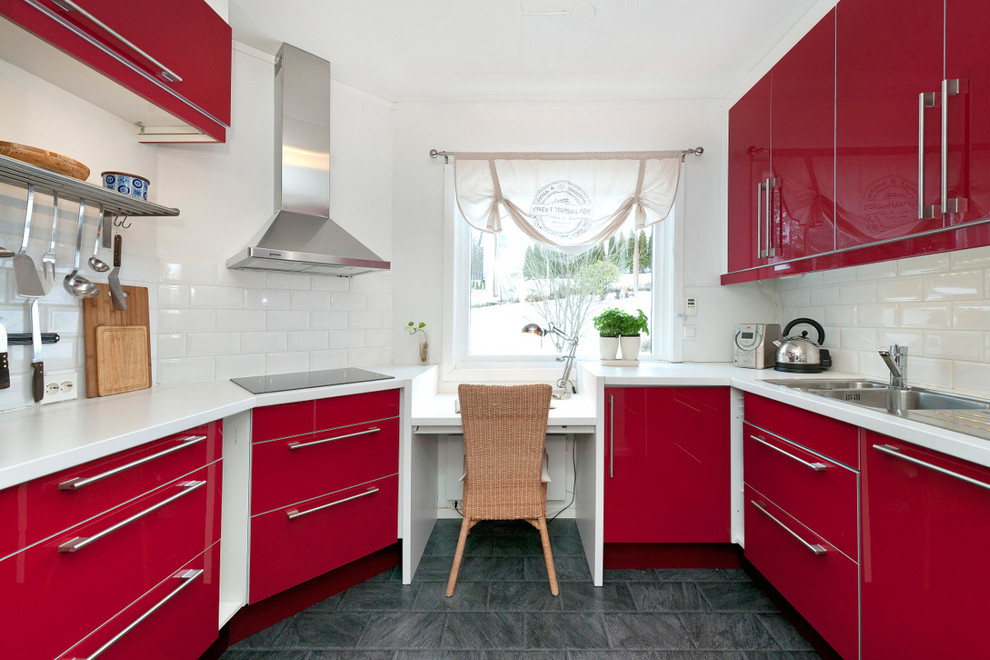 Bild på ett avskilt, litet funkis u-kök, med en dubbel diskho, släta luckor, röda skåp, laminatbänkskiva, vitt stänkskydd, stänkskydd i keramik, rostfria vitvaror och betonggolv
