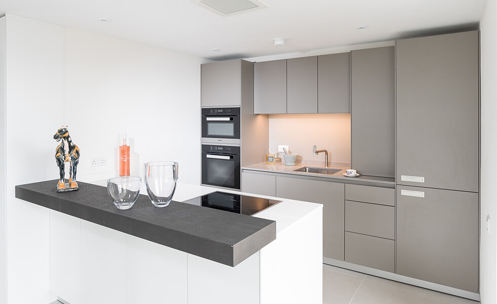 Design ideas for a small contemporary single-wall open plan kitchen in Wiltshire with an integrated sink, flat-panel cabinets, grey cabinets, composite countertops, glass tiled splashback, stainless steel appliances, porcelain flooring and an island.