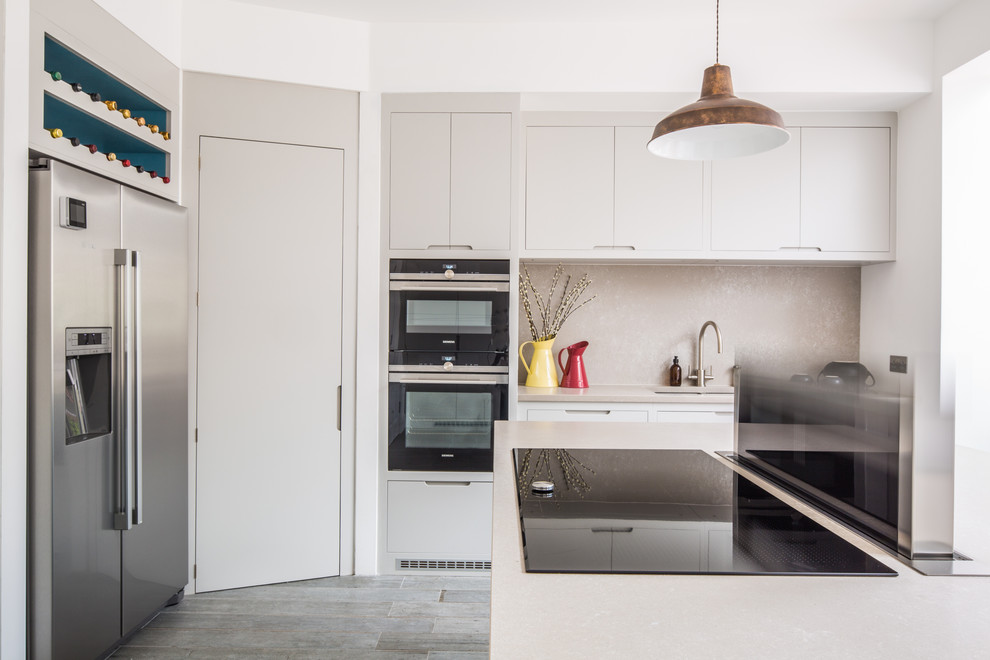 This is an example of a medium sized contemporary u-shaped open plan kitchen in London with a double-bowl sink, flat-panel cabinets, engineered stone countertops, stone slab splashback, stainless steel appliances, porcelain flooring, an island and grey floors.